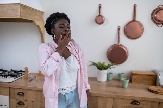 Een vrouw met een donkere huid die in de keuken staat te gapen