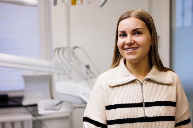 Een vrouw met een glimlach op haar gezicht met beugels op haar tanden wacht in de tandartspraktijk op haar arts. Kabinet in een moderne tandheelkundige kliniek