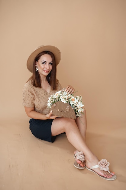 een vrouw met een hoed een shirt met madeliefjes op een beige achtergrond