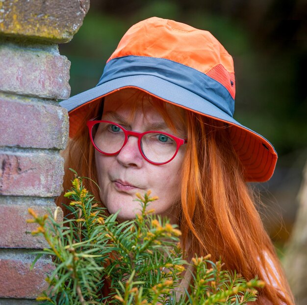 Foto een vrouw met een hoed staat achter een muur en kijkt nieuwsgierig naar de buren