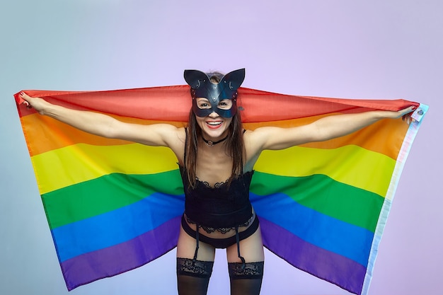 Een vrouw met een kattenmasker houdt een regenboogvlag vast.