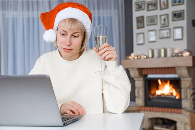 Een vrouw met een kerstmuts houdt een glas champagne vast van familieleden en vrienden op een laptop met Kerstmis