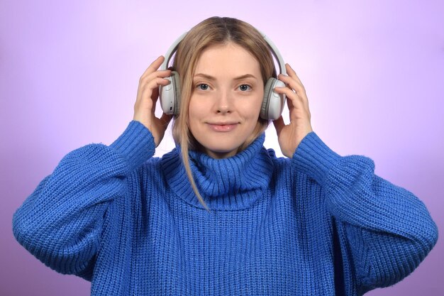 Een vrouw met een koptelefoon en een blauwe trui luistert naar muziek