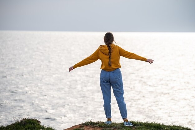 Foto een vrouw met een lange vlecht spreidt haar armen naar de zijkanten en bewondert het zeegezicht prachtig uitzicht op zee v...