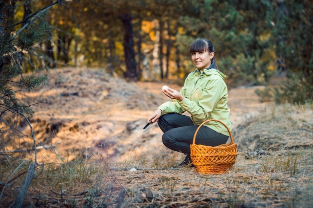 Een vrouw met een mand verzamelt paddenstoelen in het herfstbos