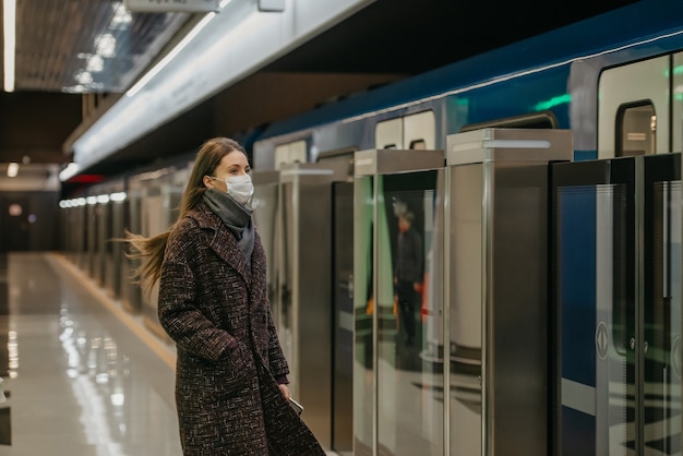 Een vrouw met een medisch gezichtsmasker om de verspreiding van het coronavirus te voorkomen, wacht op een aankomende moderne trein in de metro. Meisje met een chirurgisch masker houdt sociale afstand.