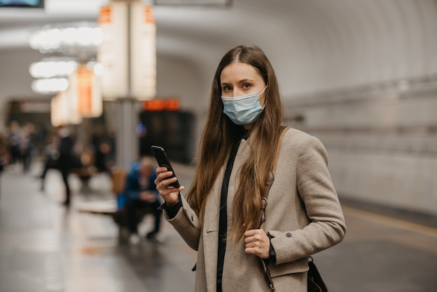 Een vrouw met een medisch gezichtsmasker om verspreiding van het coronavirus te voorkomen, houdt haar smartphone vast bij een metrostation. Een meisje met een chirurgisch gezichtsmasker tegen COVID-19 wacht op een metroplatform.