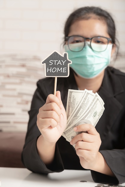 Een vrouw met een medisch masker en een zwart pak met het symbool stay home