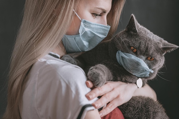 Een vrouw met een medisch masker houdt een Britse kat in haar armen, de kat heeft ook een medisch masker