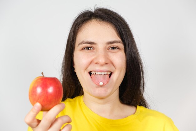 Een vrouw met een pil op haar tong houdt een appel vast