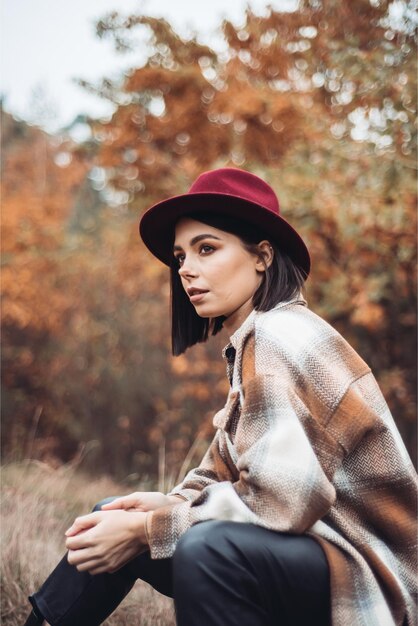 Een vrouw met een rode hoed zit in het bos en kijkt in de verte.