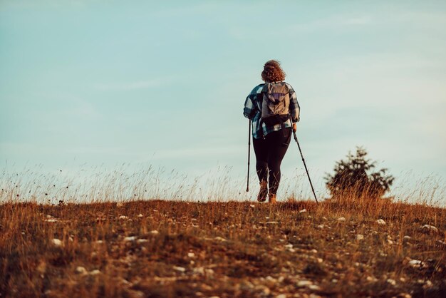 Een vrouw met een rugzak op haar rug en een berguitrusting die bij zonsondergang op de top van een berg loopt