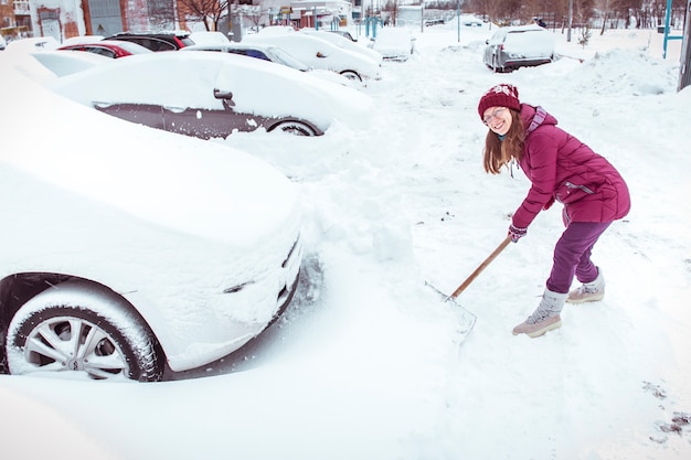 Een vrouw met een schop reinigt de sneeuw in de buurt van de auto