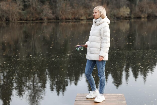 Een vrouw met een skateboard loopt in een herfstpark aan de rivier, leert schaatsen en brengt het weekend door in de frisse lucht. Gezond Sportconcept.