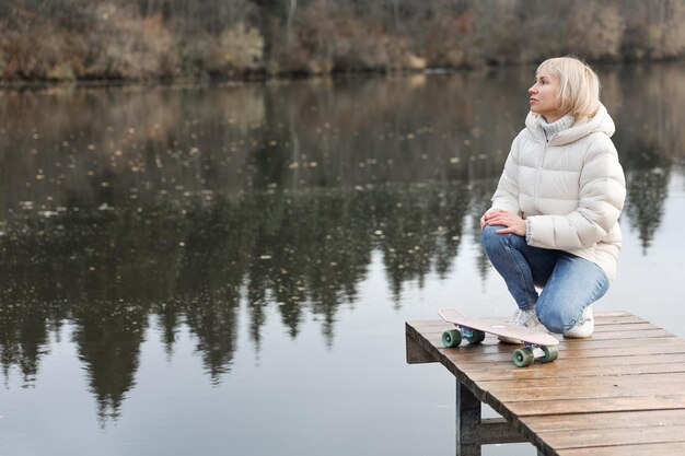 Foto een vrouw met een skateboard loopt in een herfstpark bij de rivier en leert schaatsen tijdens een weekendje weg