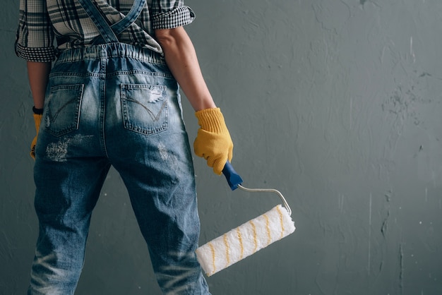 Een vrouw met een sterke wil in een bouwhelm, wanten, bril en overalls is thuis bezig met reparatie- en bouwwerkzaamheden. concept van een sterke en onafhankelijke vrouw