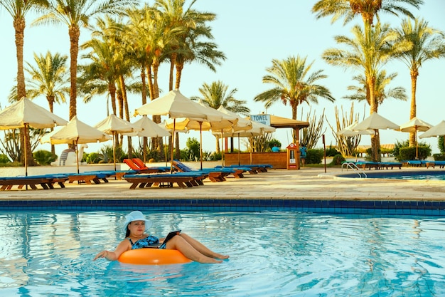 Een vrouw met een zonnehoed in het zwembad in een zwemkring met een laptop werkt op afstand op de achtergrond