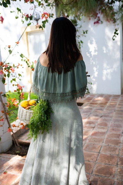 Een vrouw met haar rug naar haar toe loopt met een mand met groenten en fruit in de achtertuin