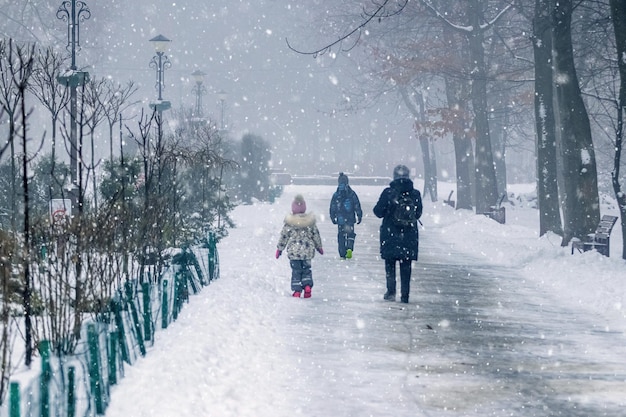 Een vrouw met kinderen op een wandeling in een winterpark tijdens sneeuwval