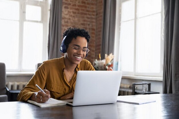 een vrouw met koptelefoon zit aan een tafel met een laptop en een pen in haar hand