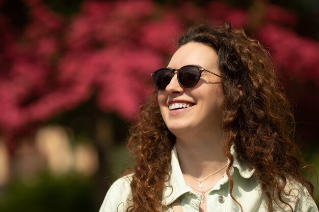 Een vrouw met krullend haar glimlacht voor een bos roze bloemen