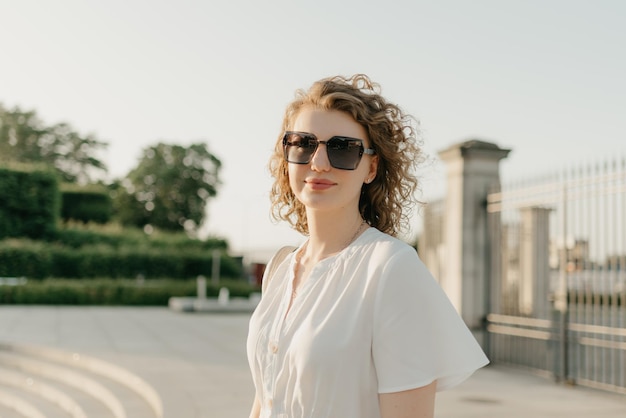 Een vrouw met krullend haar in zonnebril poseert in het park