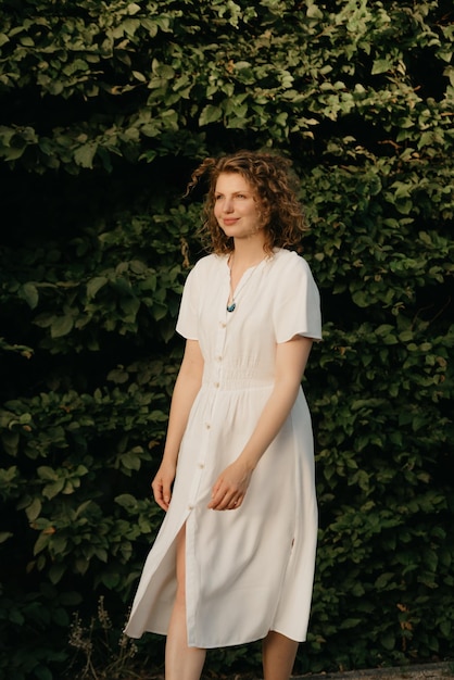 Een vrouw met krullend haar poseert 's avonds in de tuin