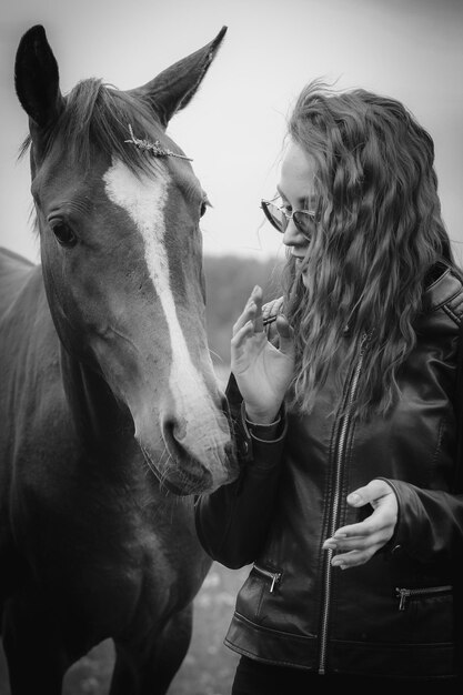 Een vrouw met lang haar en een bril die een paard aait.