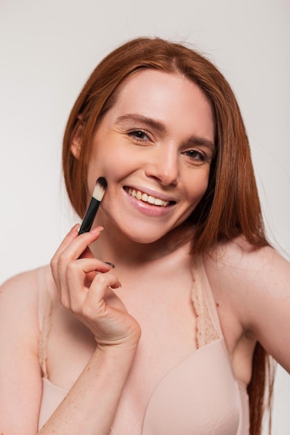 Een vrouw met rood haar brengt make-up aan.