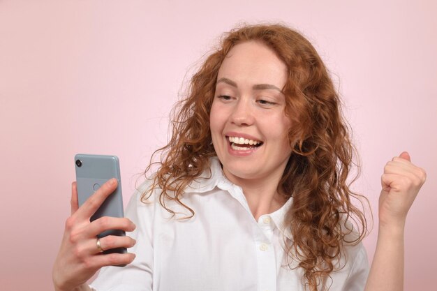 Een vrouw met rood haar kijkt naar een telefoon en glimlacht.