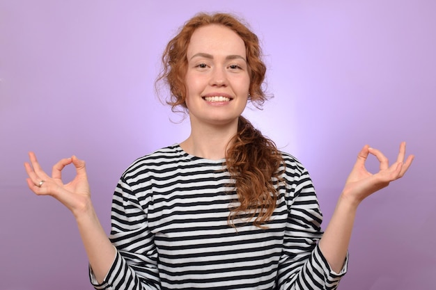 Een vrouw met rood haar mediteert voor een paarse achtergrond.