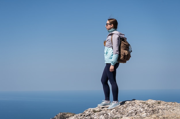 Een vrouw met zonnebril staat op een hoge berg en geniet van het uitzicht op de eindeloze blauwe zee sea