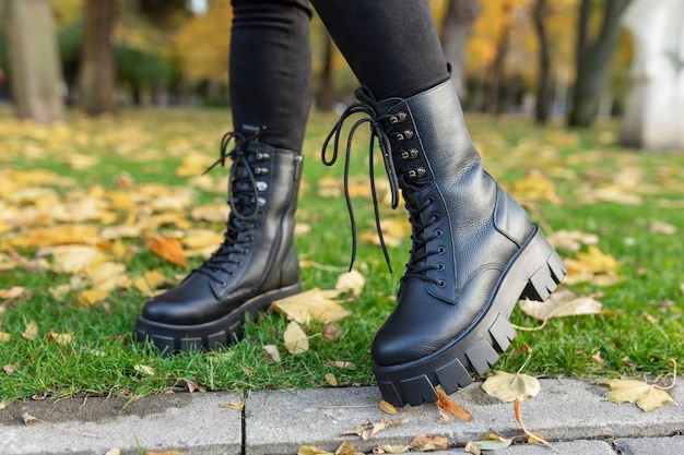 Een vrouw met zwarte laarzen staat in de herfst in het gras.