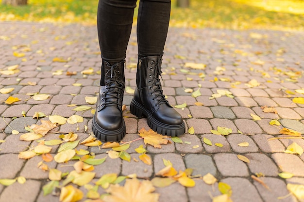 Een vrouw met zwarte laarzen staat op een bakstenen loopbrug met gevallen bladeren op de grond.