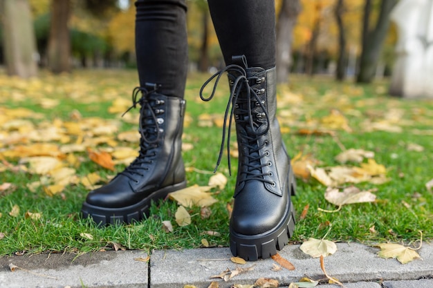 Een vrouw met zwarte leren laarzen staat op het gras in een park.