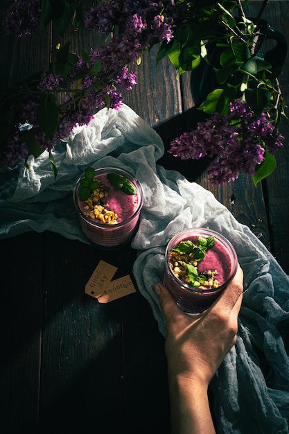 Een vrouw neemt een glas met een bramen-smoothie op tafel met lila