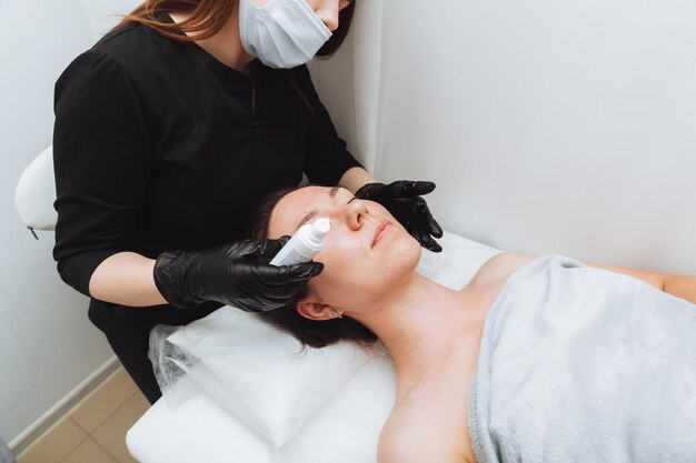 Een vrouw ondergaat een cosmetische ingreep in de salon spa. De schoonheidsspecialist brengt de crème aan op het gezicht van het meisje