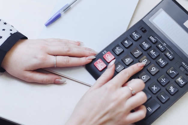 Een vrouw overweegt op een rekenmachine de kosten, inkomsten, uitgaven. Verdeling van het gezinsbudget. Zakenvrouwen houdt zich bezig met boekhouding