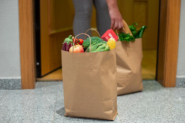 Een vrouw pakt een zak eten bij de deur van haar huis Coronavirus Quarantaine Blijf thuis Online winkelen Groenten en fruit bezorgen tijdens quarantaine en zelfisolatie