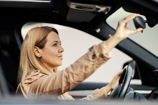 Een vrouw past de achteruitkijkspiegel aan terwijl ze in haar auto zit