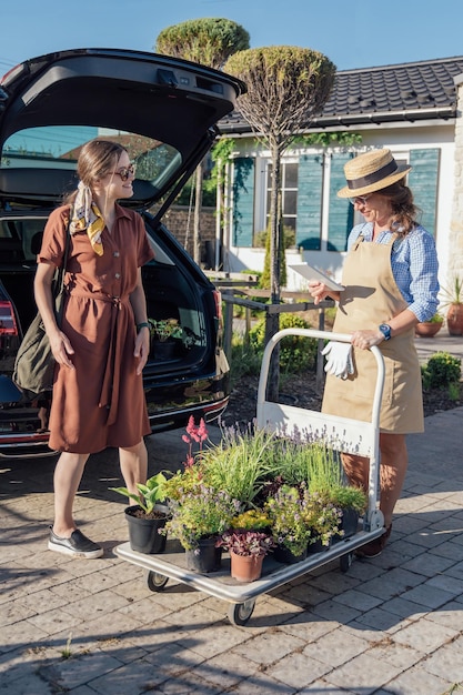 Een vrouw raadpleegt een vrouwelijke tuinman over planten voordat ze ze koopt in een tuincentrum in de buurt van de auto