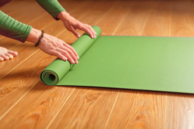 Een vrouw rolt een groene mat uit voor een yogales