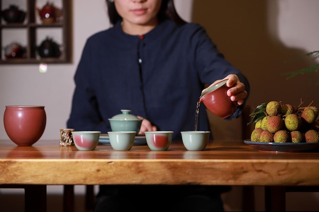 Een vrouw schenkt een kopje thee in op een houten tafel.