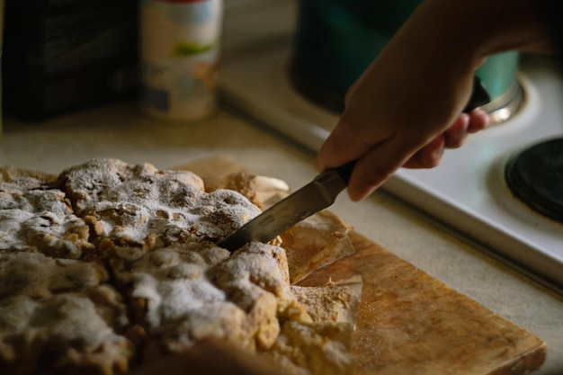 Een vrouw snijdt met de hand een afgewerkte Charlotte-appeltaart in gelijke stukken met een mes in de keuken