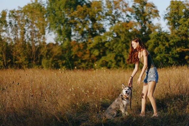 Een vrouw speelt en danst met een husky hond in de natuur in de herfst op een grasveld en glimlacht op een goede avond in de ondergaande zon Hoogwaardige foto