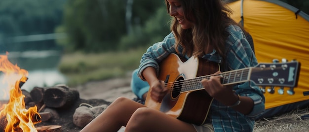 Een vrouw speelt haar gitaar bij een kampvuur omringd door de rustige sfeer aan de oever van een rivier bij zonsondergang