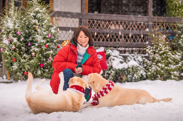 Een vrouw speelt met labradorsmi-honden in de buurt van een versierde kerstboom tijdens een sneeuwval in de winter op de binnenplaats van een flatgebouw.