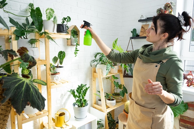 Een vrouw spuit uit een spuitpistool huisplanten uit haar collectie die met liefde zijn gekweekt op planken in het interieur van het huis Thuisplanten groeien kas waterhuishouding bevochtiging