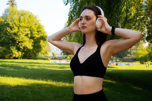 een vrouw staat en luistert naar muziek in een koptelefoon en drinkt vrolijk na een wandeling in het park