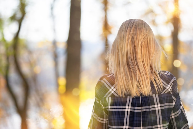 Een vrouw staat met haar rug tegen de achtergrond van de herfst